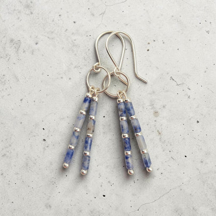 Bijou by SAM Stone Creek earrings with blue spot jasper tube beads and sterling silver hoops on a grey background.