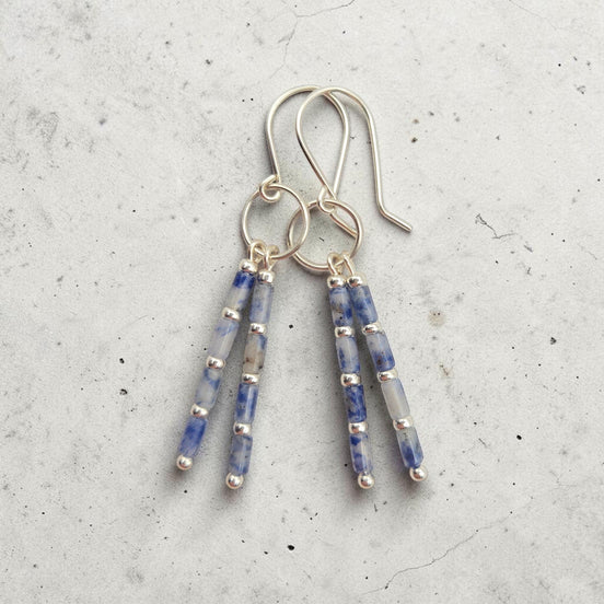 Bijou by SAM Stone Creek earrings with blue spot jasper tube beads and sterling silver hoops on a grey background.