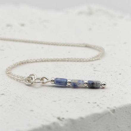 Bijou by SAM Stone Creek necklace featuring blue spot jasper tube beads and sterling silver chain on white stone.