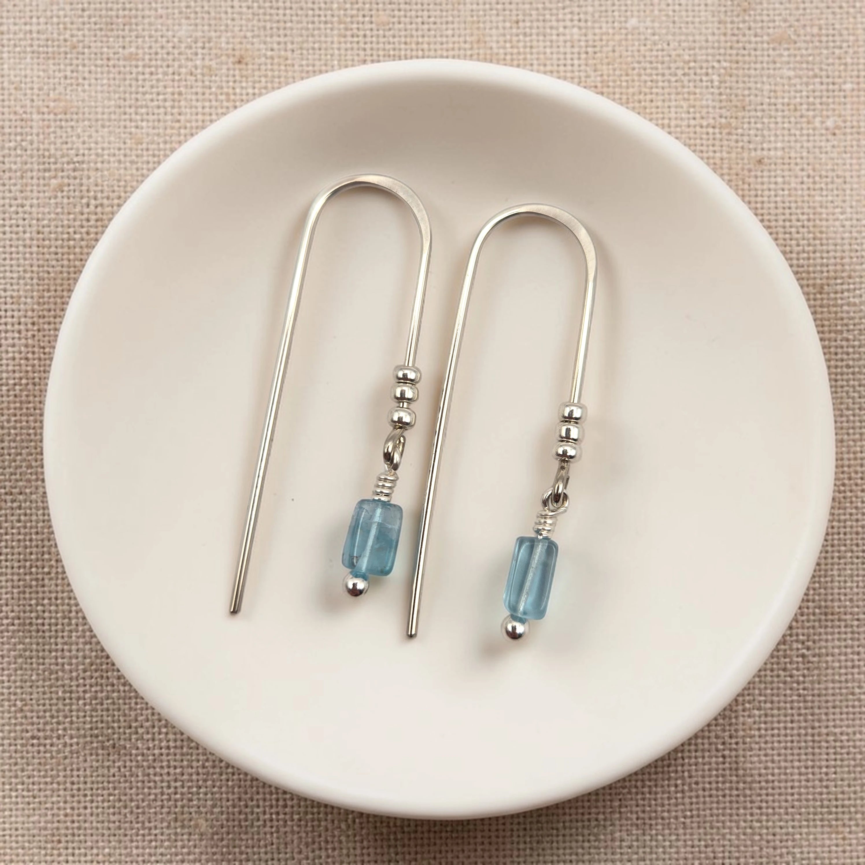 Silver earrings with blue beads on a white dish
