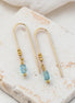 Gold earrings with blue beads on a marble surface