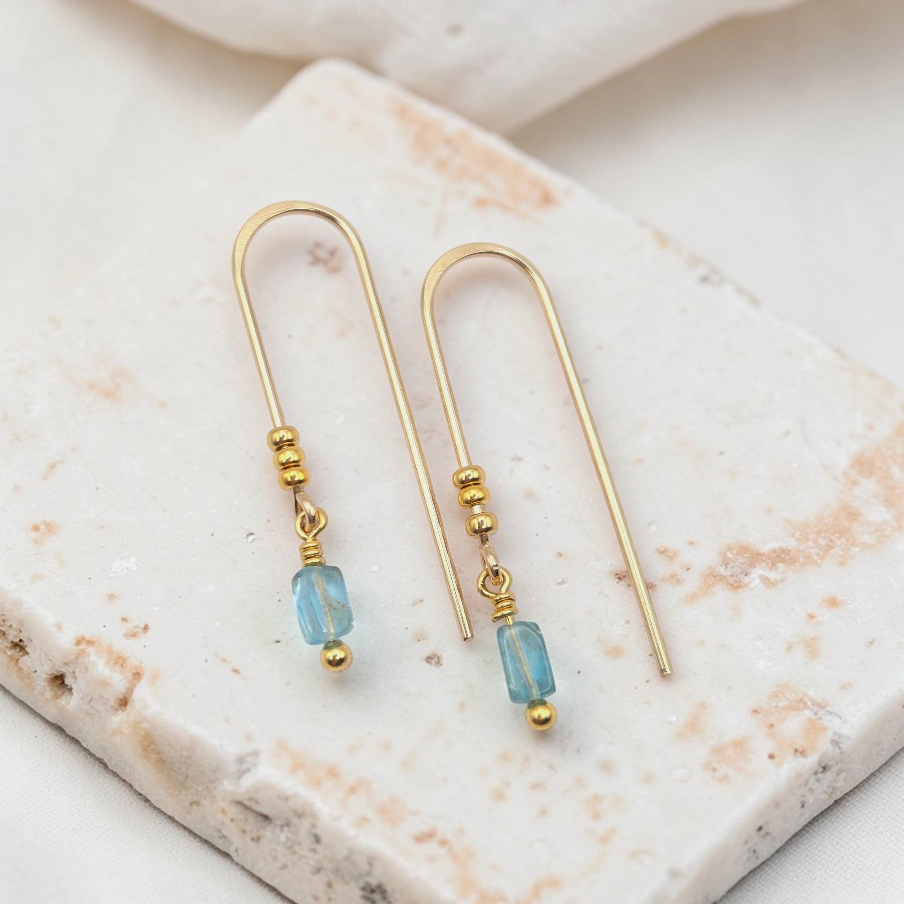 Gold earrings with blue beads on a marble surface