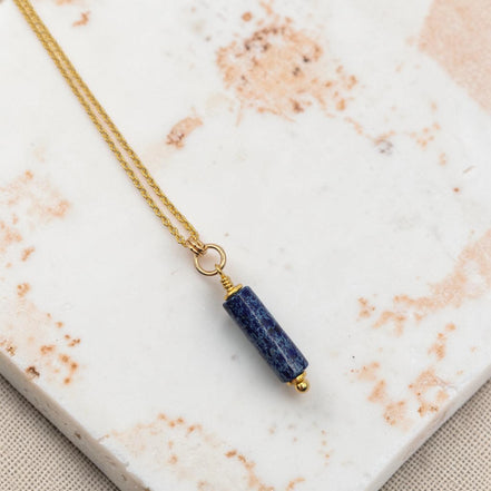 Necklace with a blue cylindrical pendant on a marble surface