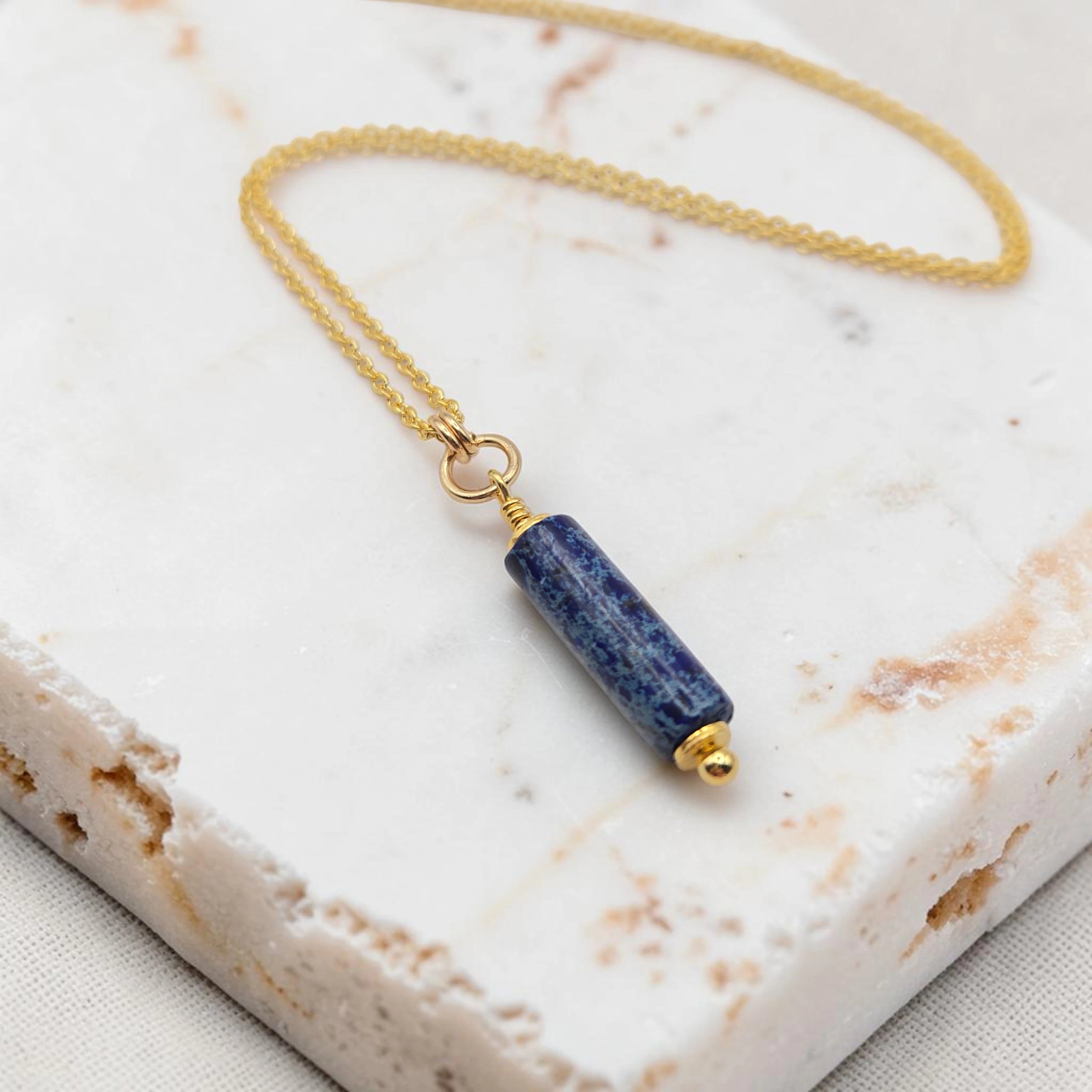 Necklace with a blue cylindrical pendant on a marble surface
