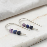 Silver earrings with purple and blue beads on a marble surface