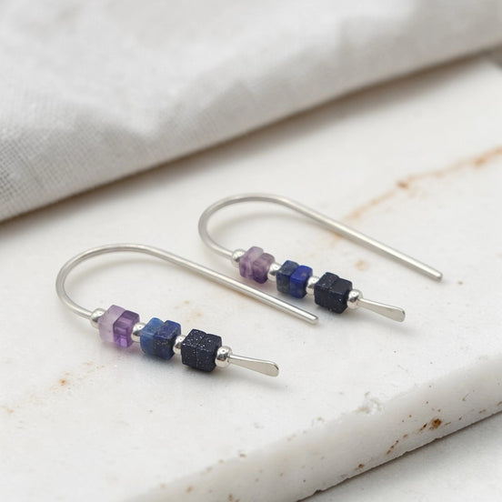 Silver earrings with purple and blue beads on a marble surface