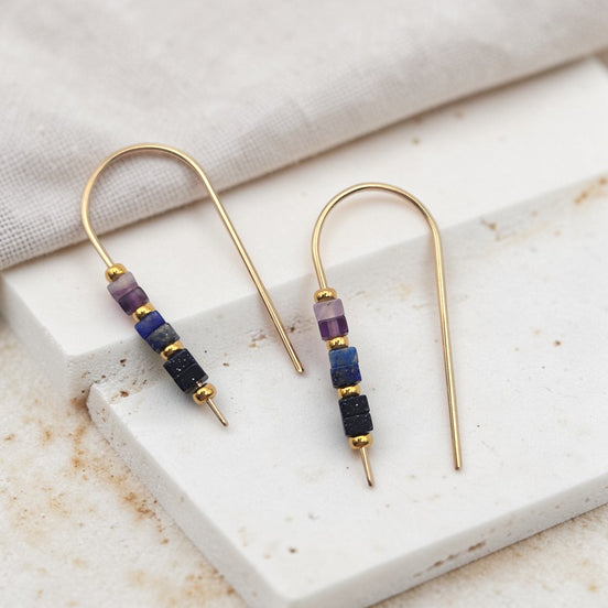 Pair of gold earrings with colorful beads on a marble surface