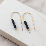 Pair of gold earrings with black beads on a marble surface