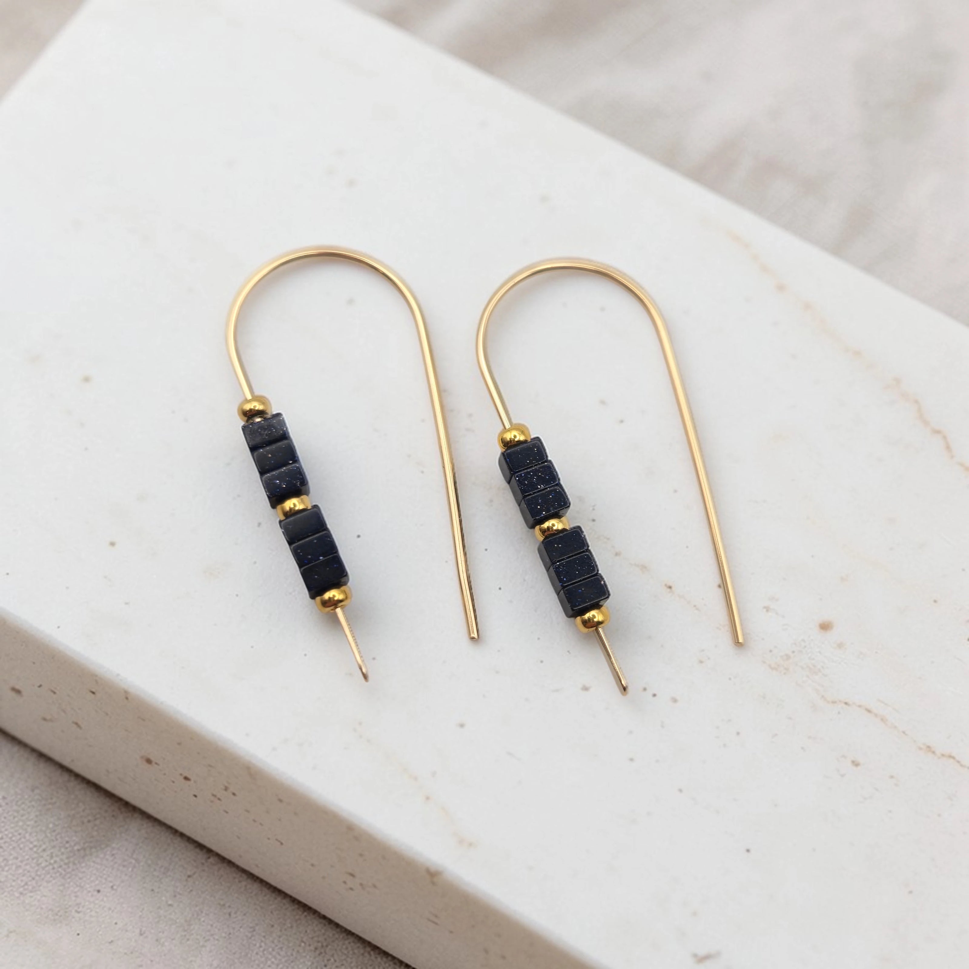 Pair of gold earrings with black beads on a marble surface