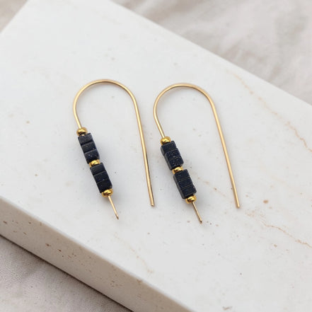 Pair of gold earrings with black beads on a marble surface