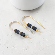 Gold earrings with black beads on a light gray surface