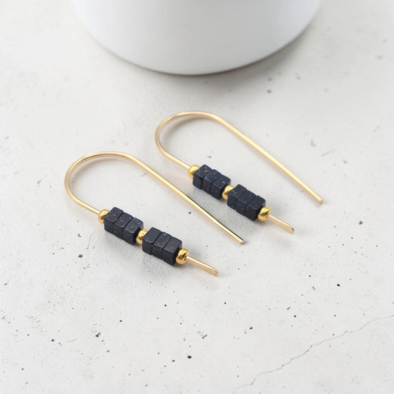 Gold earrings with black beads on a light gray surface