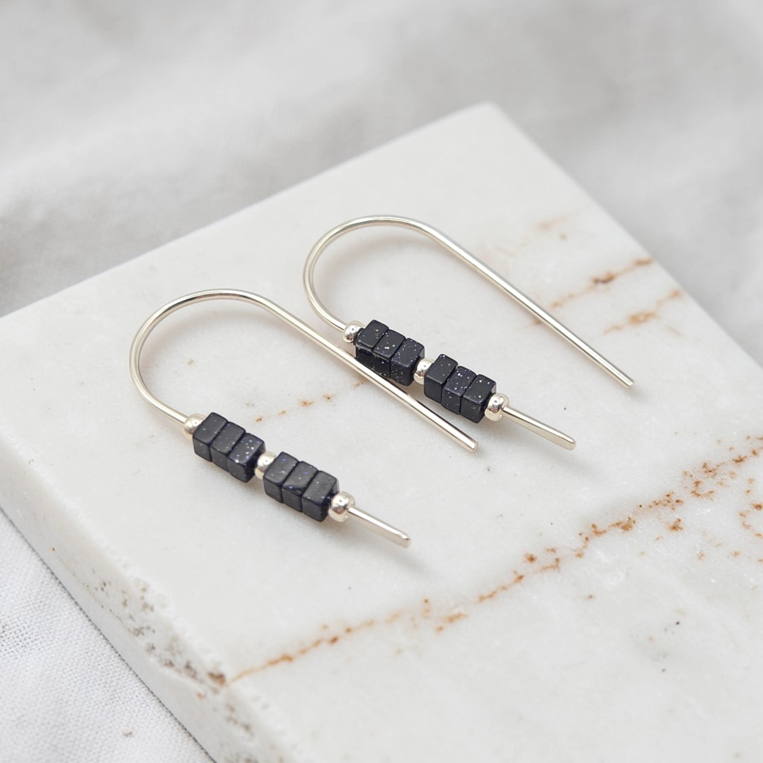 Silver earrings with black beads on a marble surface