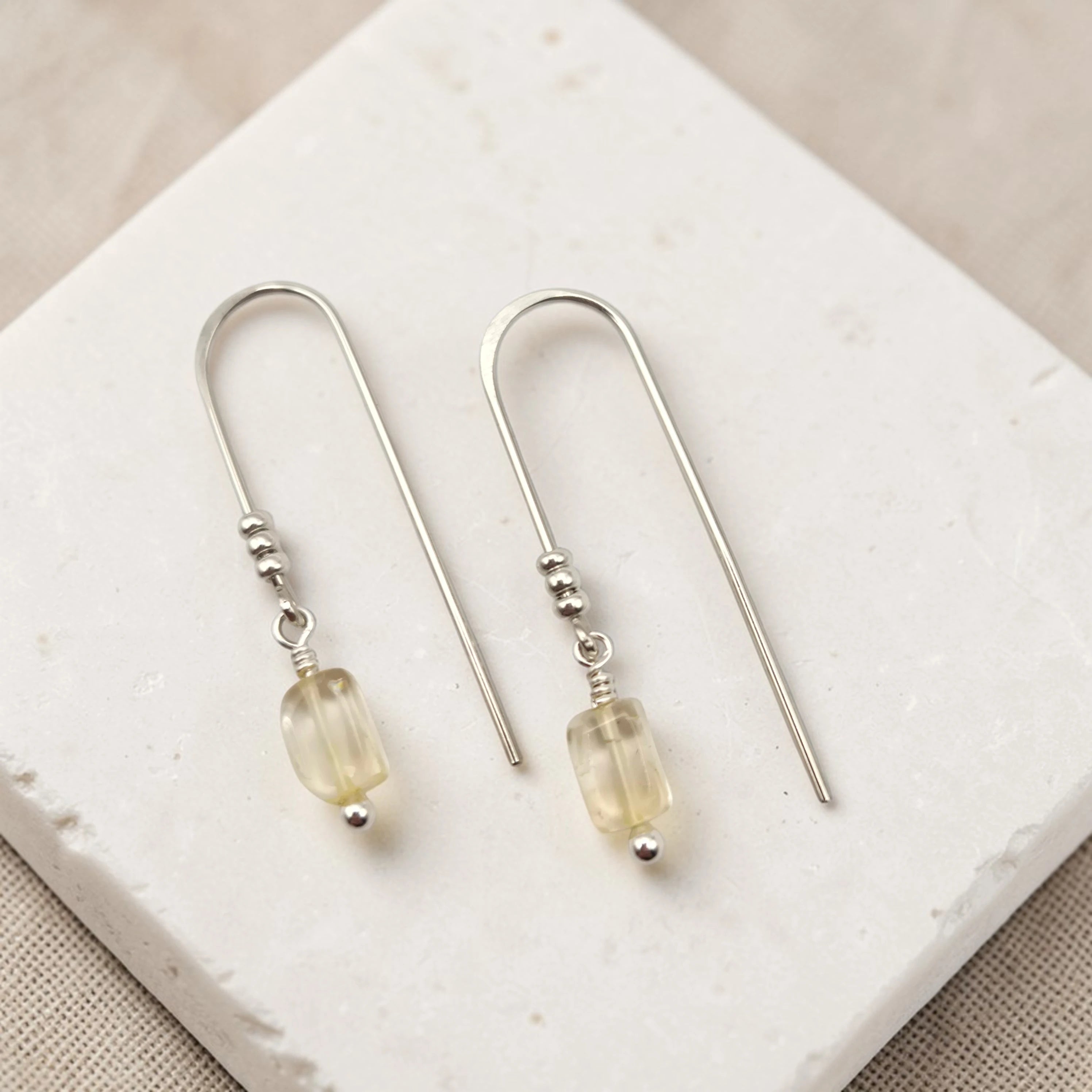 Silver earrings with citrine beads on a white stone surface