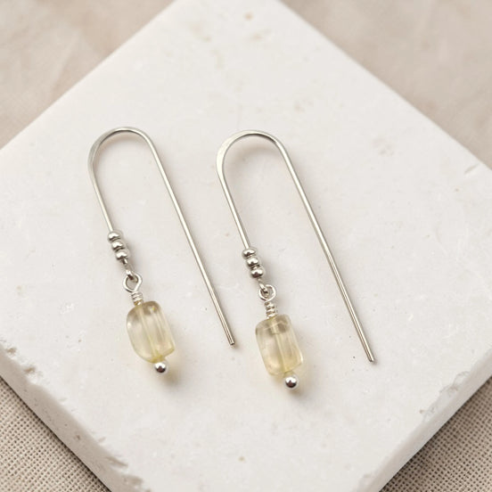 Silver earrings with citrine beads on a white stone surface