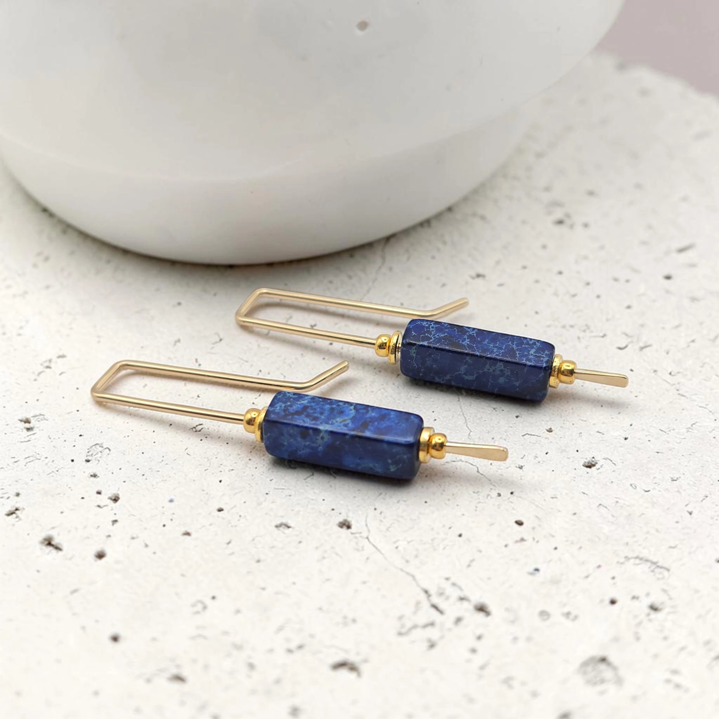 Pair of gold and blue earrings on a textured surface with a blurred background