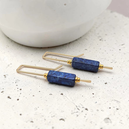 Pair of gold and blue earrings on a textured surface with a blurred background