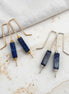 Pair of blue stone earrings with gold and silver hooks on a marble surface.