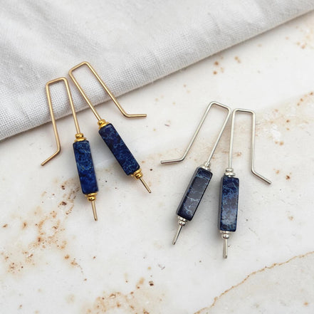 Pair of blue stone earrings with gold and silver hooks on a marble surface.