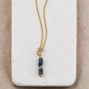 Gold necklace with a blue pendant on a marble surface