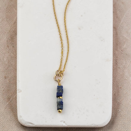Gold necklace with a blue pendant on a marble surface
