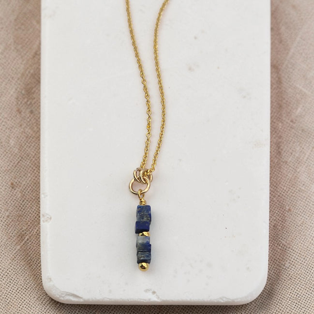 Gold necklace with a blue pendant on a marble surface