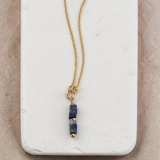 Gold necklace with a blue pendant on a marble surface