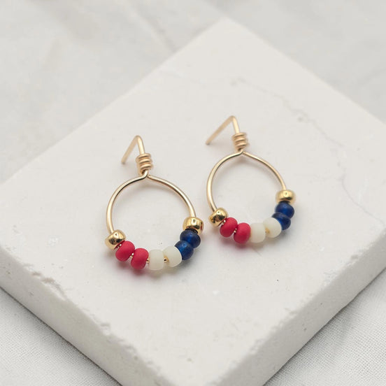 Gold hoop earrings with red white and blue beads on a white surface