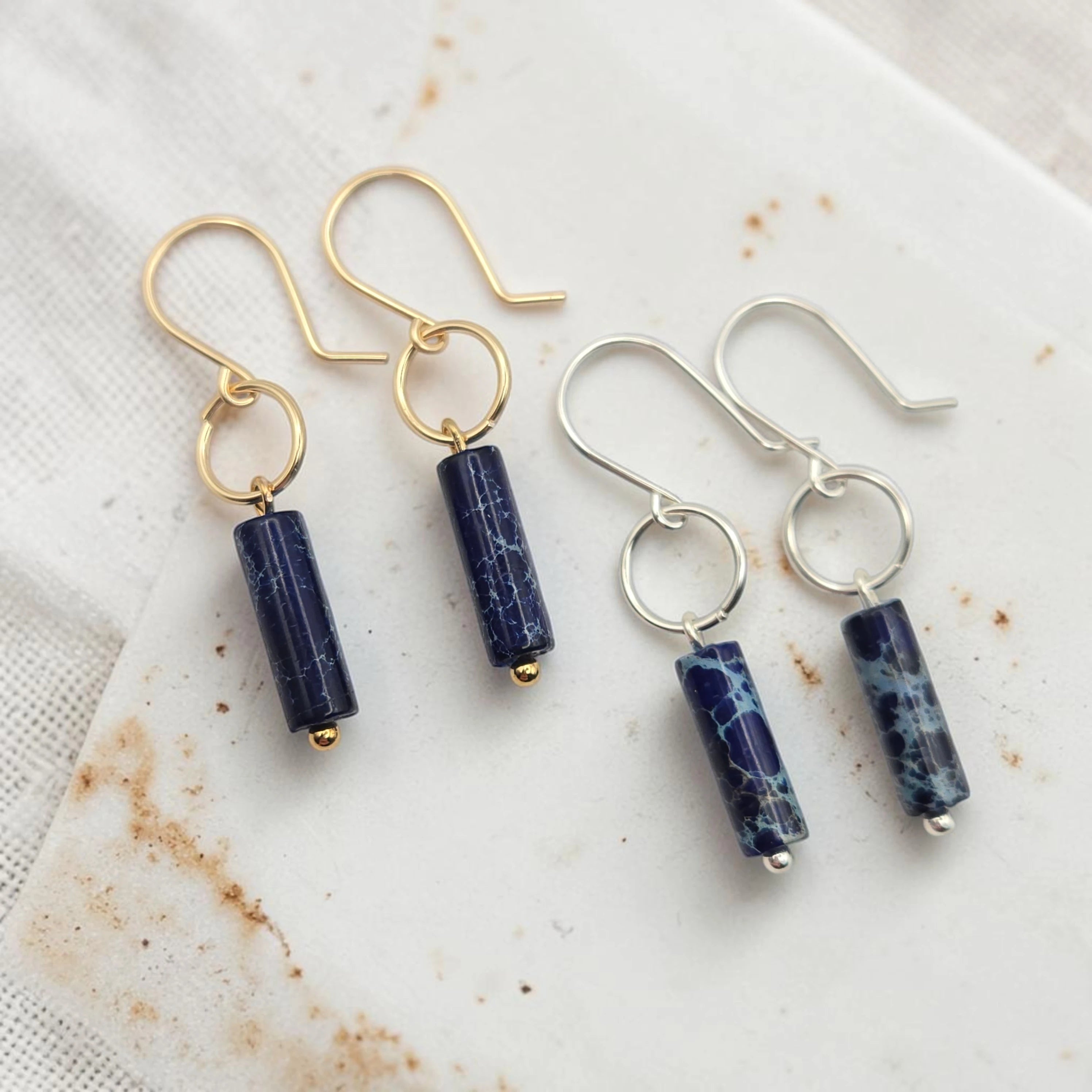 Two pairs of earrings with blue cylindrical beads on a marble surface