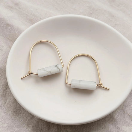 Pair of earrings with marble-like beads on a white dish