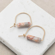 Gold hoop earrings with marbled pink and white stones on a marble surface
