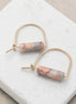Gold hoop earrings with marbled pink and white stones on a marble surface