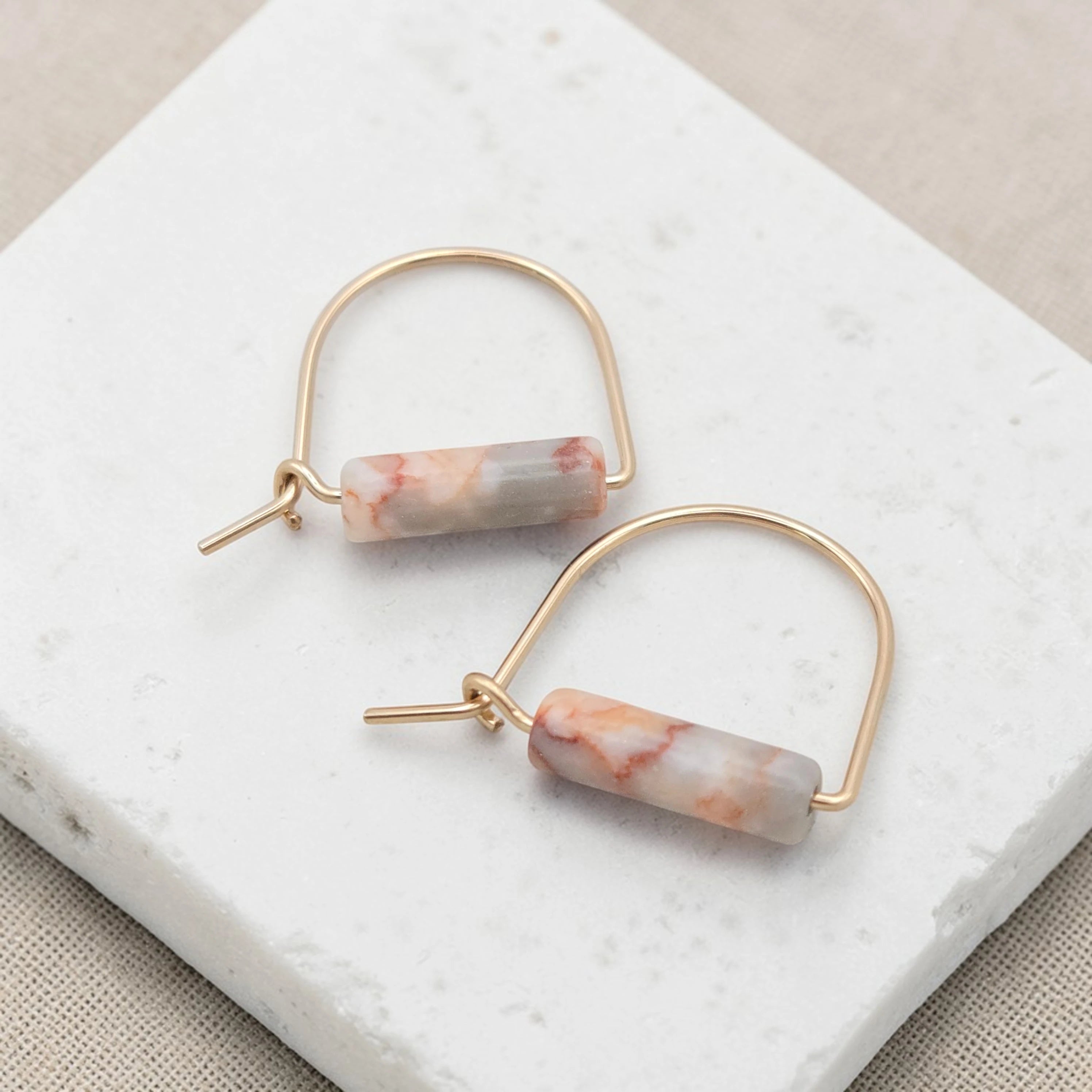 Gold hoop earrings with marbled pink and white stones on a marble surface