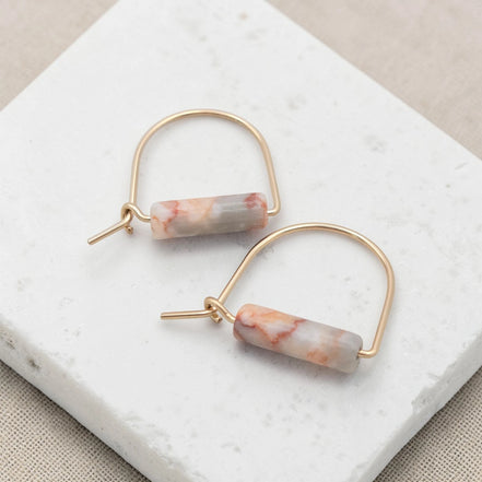 Gold hoop earrings with marbled pink and white stones on a marble surface