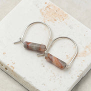 Pair of hoop earrings with cylindrical stone beads on a marble surface