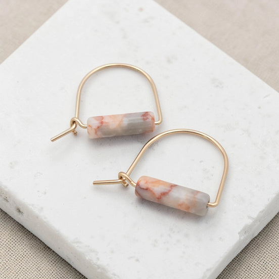 Gold hoop earrings with marbled pink and white stones on a marble surface