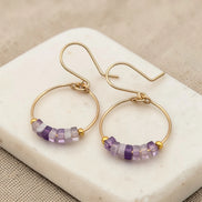 Gold hoop earrings with amethyst  purple beads on a marble surface