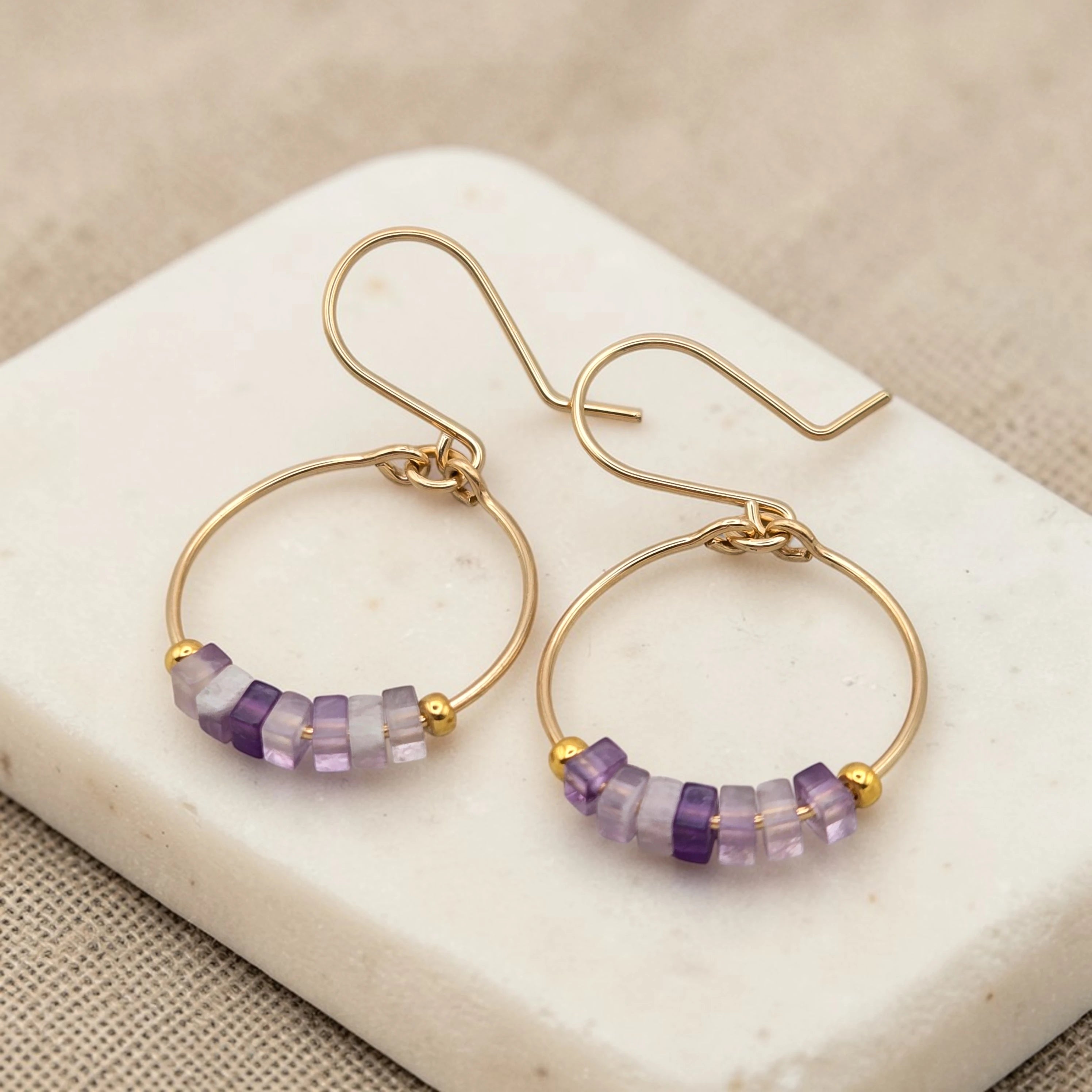 Gold hoop earrings with amethyst  purple beads on a marble surface
