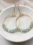 Gold hoop earrings with aquamarine blue beads on a white dish.