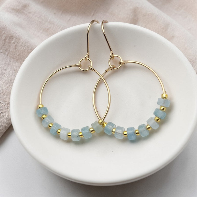 Gold hoop earrings with aquamarine blue beads on a white dish.