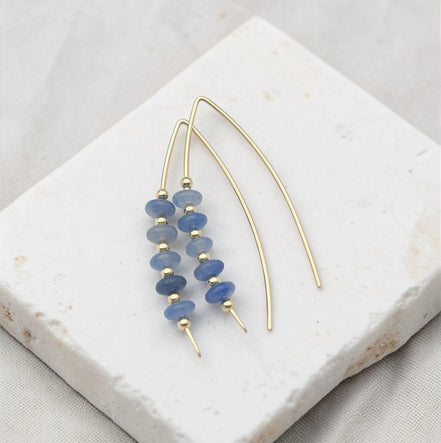 Gold and blue beaded earrings on a textured surface