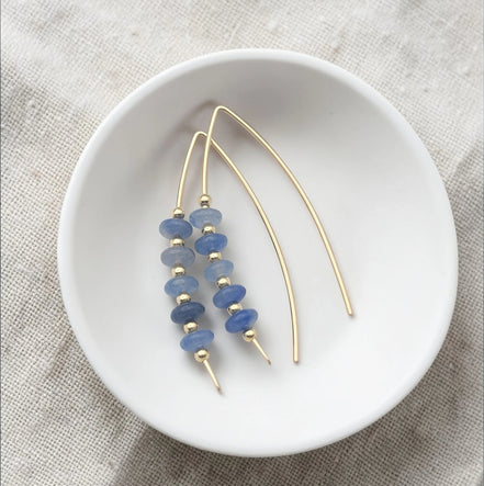 Gold and blue beaded earrings on a white dish with a beige fabric background