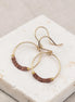 Gold hoop earrings with brown beads on a marble surface