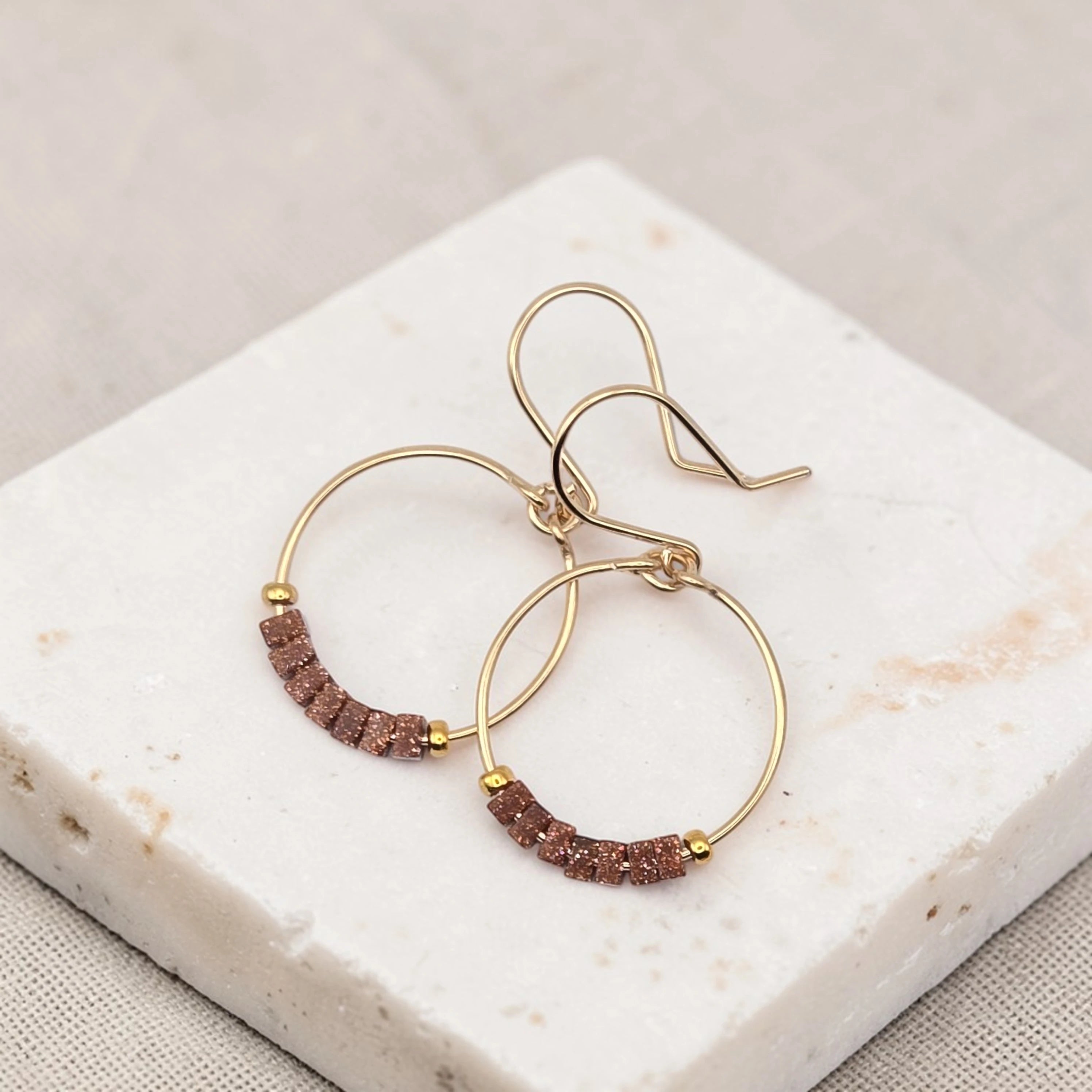 Gold hoop earrings with brown beads on a marble surface