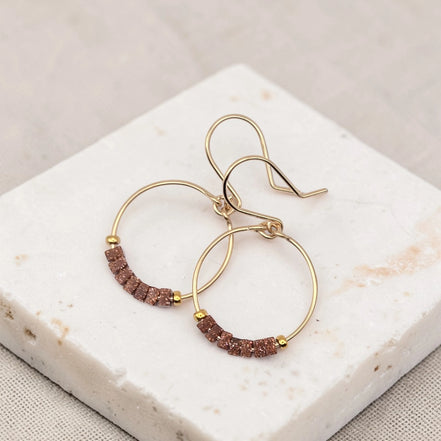 Gold hoop earrings with brown beads on a marble surface
