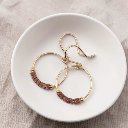Gold hoop earrings with brown beads on a white dish.