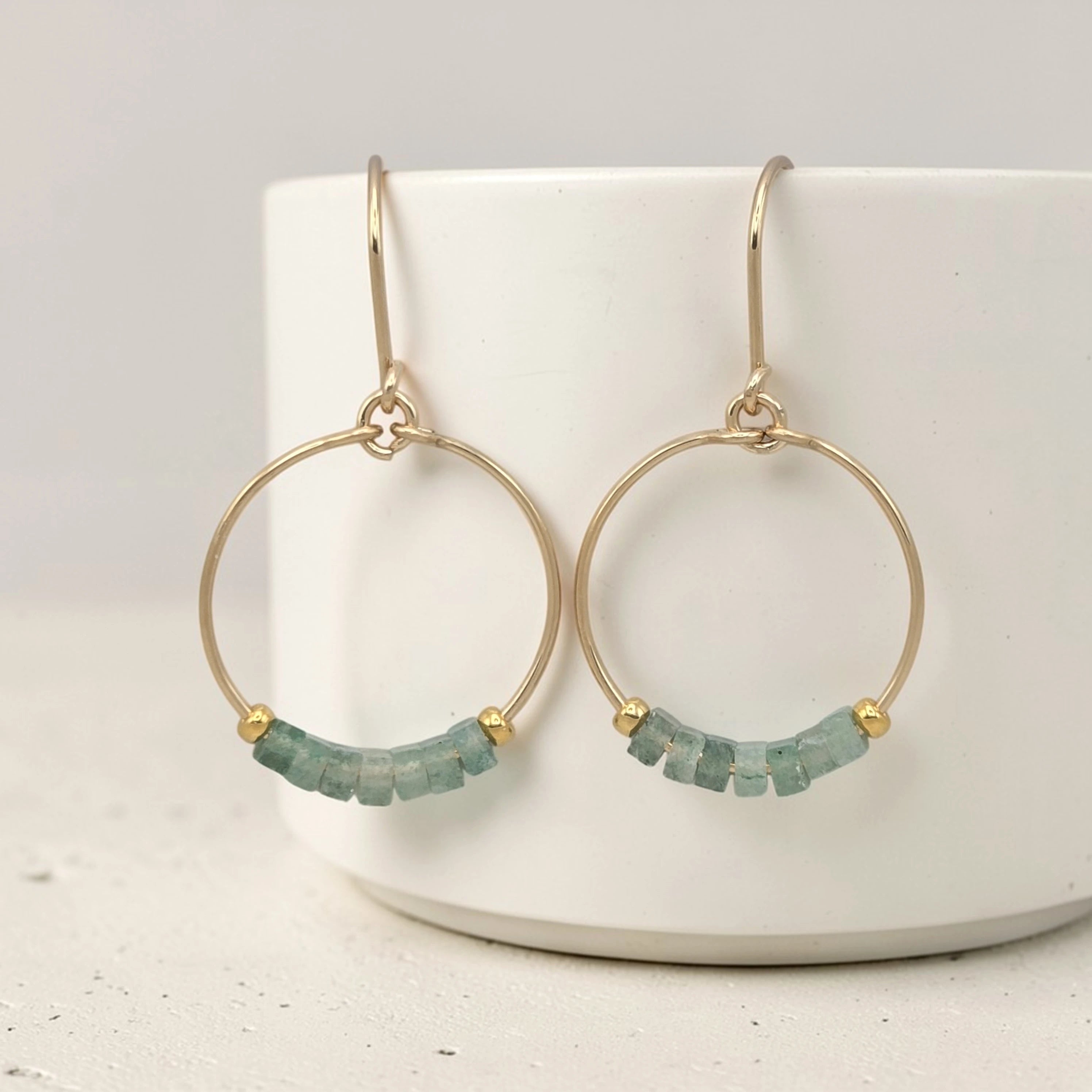 Gold hoop earrings with green aventurine beads on a white surface