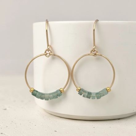Gold hoop earrings with green aventurine beads on a white surface