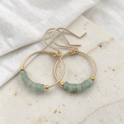 Gold hoop earrings with green aventurine beads on a marble surface