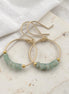 Gold hoop earrings with green aventurine beads on a marble surface
